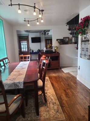 A dining area with a wooden table and chairs, a rug, a television, and a staircase with a railing.