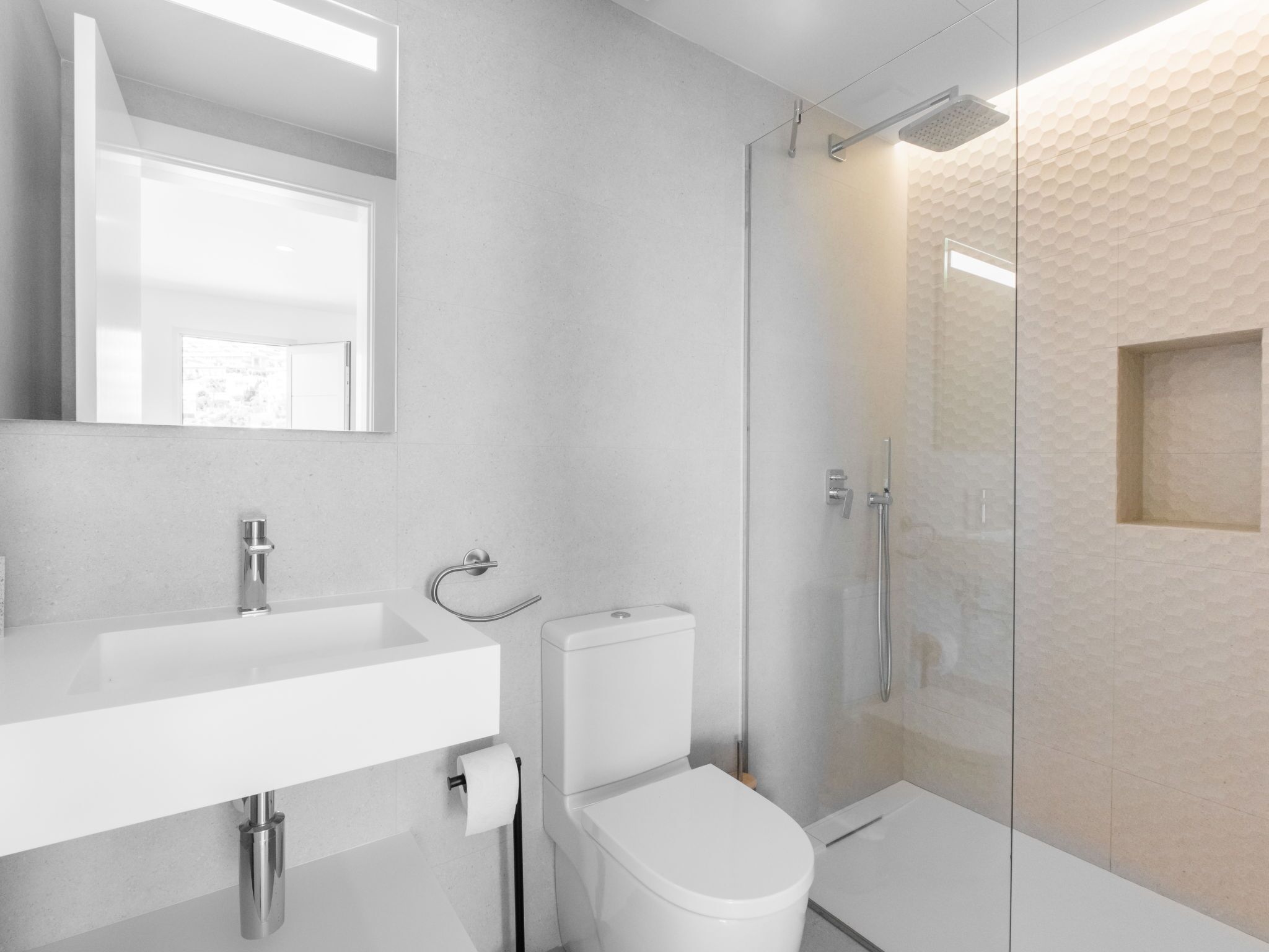 Un baño moderno con cabina de ducha de vidrio, un lavabo blanco y un inodoro.