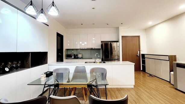 A modern kitchen with white cabinetry, a central island, stainless steel appliances, and a glass dining table with chairs.