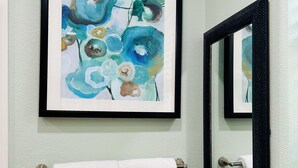 A bathroom with a framed abstract painting, two white towels on a towel rack, and a mirror with a black frame. - Chic Casita with AC, WiFi in peaceful Coachella (Coachella)