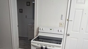 A kitchen with a white stove, a checkered mat, and a door to a bathroom. - The C&C
Comfort and Convenience (Milwaukee)