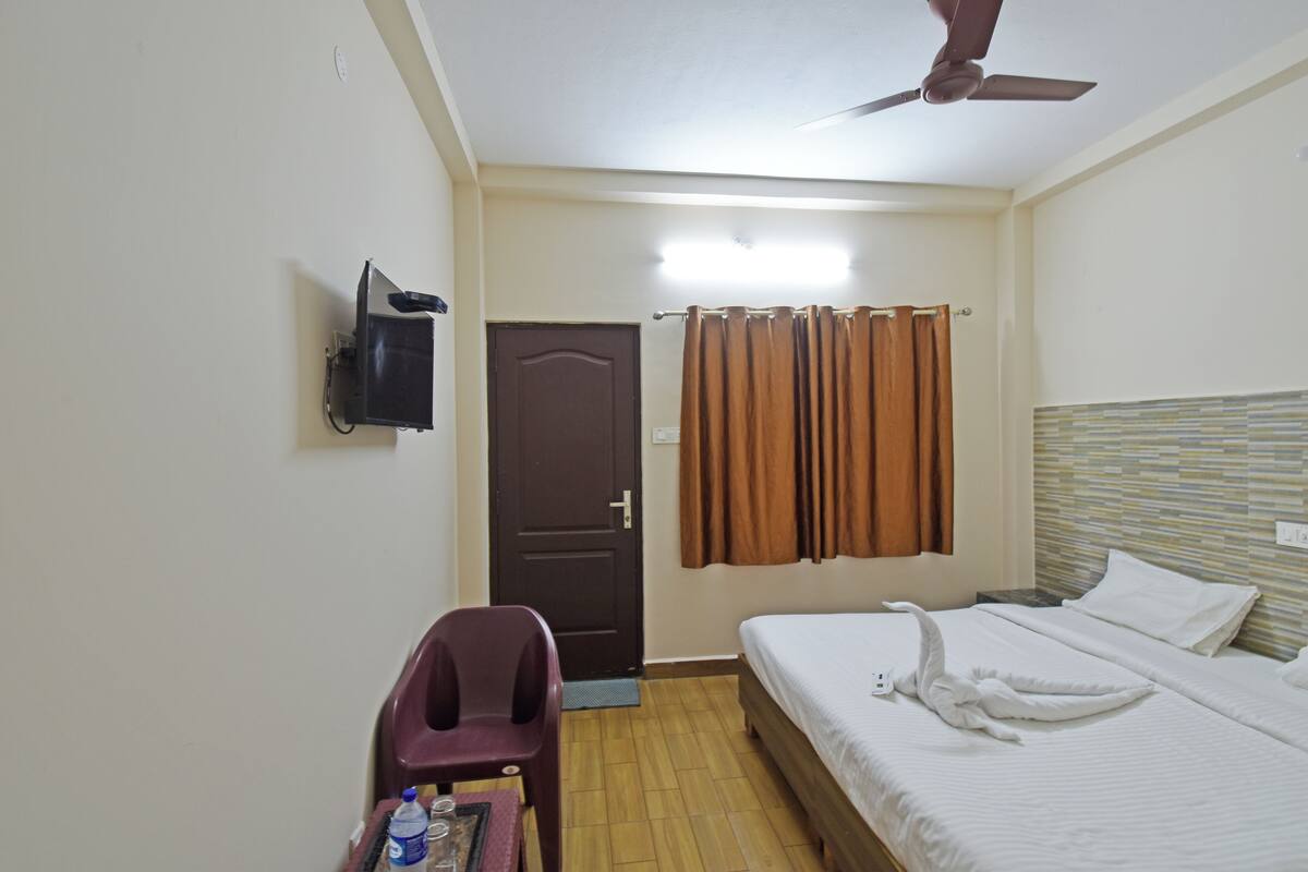 Une chambre d’hôtel comprenant un lit, un bureau avec une chaise, une télévision, une porte et un ventilateur de plafond.