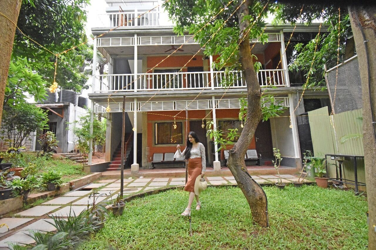 A two-story building with a balcony, surrounded by greenery and potted plants.
