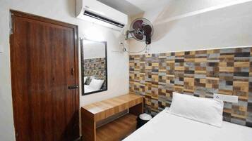 Un dormitorio con un armario de madera, una mesita de noche, un espejo, una cama con ropa blanca y un aire acondicionado de pared.
