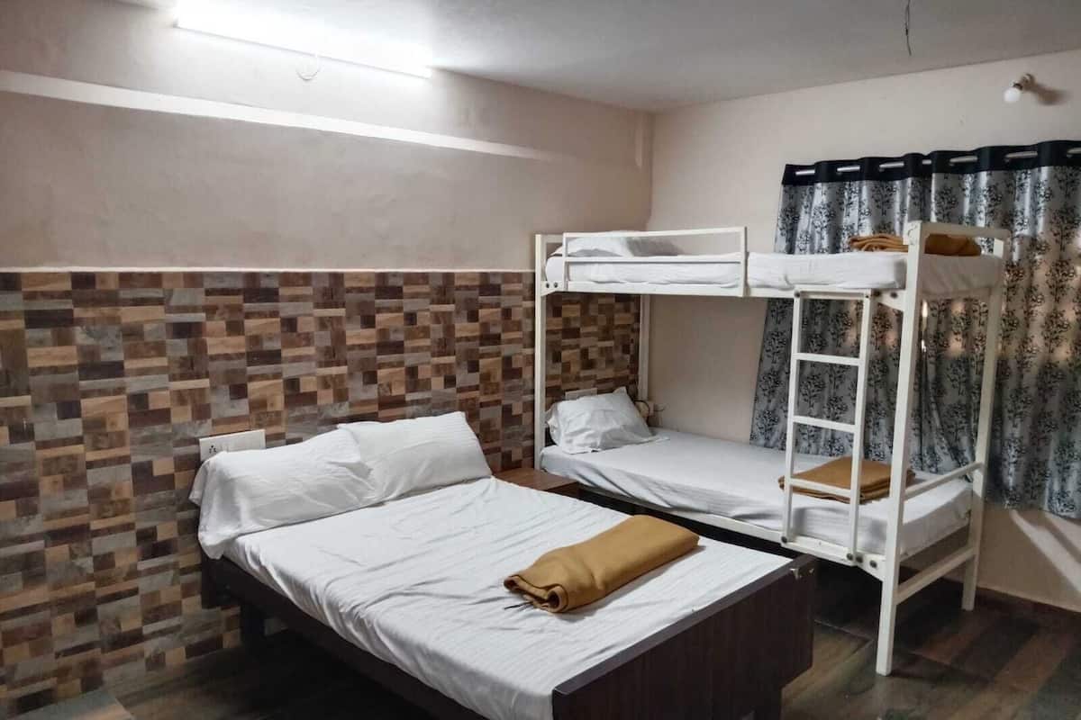 Une chambre avec deux lits superposés, une tête de lit en bois, un mur décoré d’un motif et une fenêtre avec des rideaux.