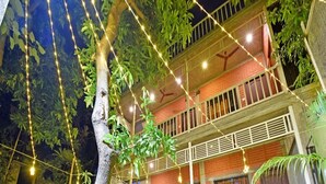 Ein zweistöckiges Gebäude mit einem Balkon, Lichterketten und Topfpflanzen.