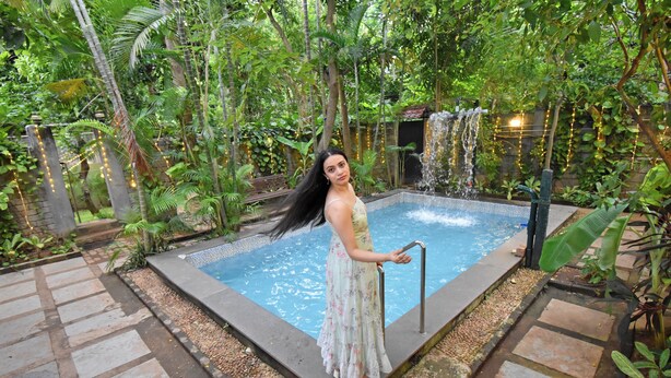 Eine Frau steht an einem Pool mit einem Wasserfall in einem üppigen, grünen Garten.