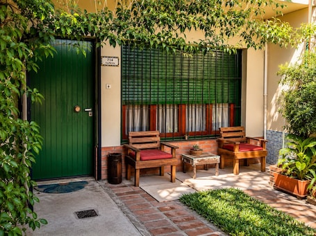 A green door with a number plate, a wooden bench with red cushions, and a small table with a potted plant.. Private Independent room, Garden View with A/C Martínez, Unicenter