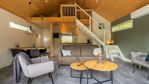 A modern loft-style living space with a wooden ceiling, a staircase, a kitchen, and a seating area with a sofa and two round tables. - Boslodge by Interhome (Hoenderloo)