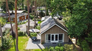 A small wooden house with a large sliding glass door, surrounded by lush greenery and a pond. - Boslodge by Interhome (Hoenderloo)