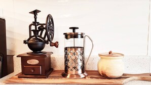 A coffee grinder, a coffee press, and a container on a wooden board.
