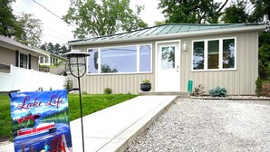 A single-story house with a green roof and beige siding, a gravel driveway, and a mailbox with the number 7195. - Lake Front Cottage | Kayaks | Game Table Fun (Shipshewana)
