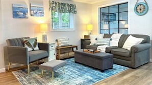 A modern living room with a grey sofa set, a small side table, a patterned rug, and a window with a view of a lake. - Lake Front Cottage | Kayaks | Game Table Fun (Shipshewana)