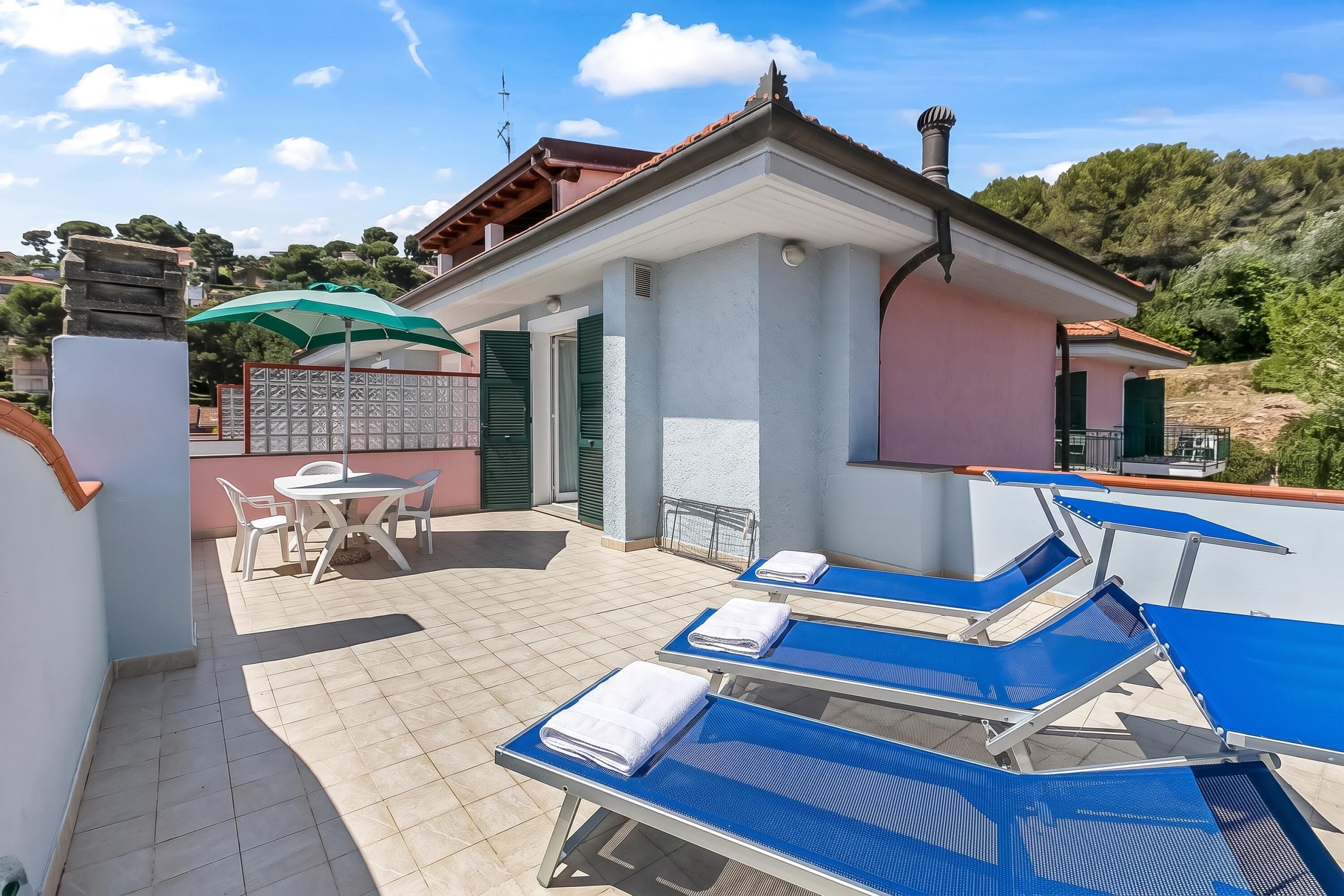 Une terrasse sur le toit avec des fauteuils de jardin bleus, une table avec des chaises et un parasol vert.