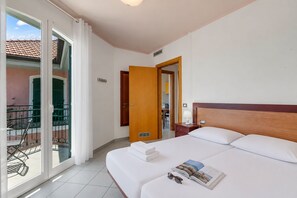 Una habitación de hotel con cama, mesita de noche, ventana con cortinas y vistas al exterior.