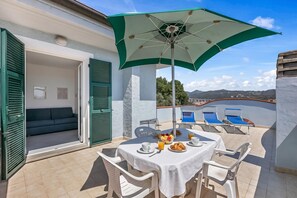Un patio con una mesa dispuesta para el desayuno, una sombrilla verde y un sofá al fondo.