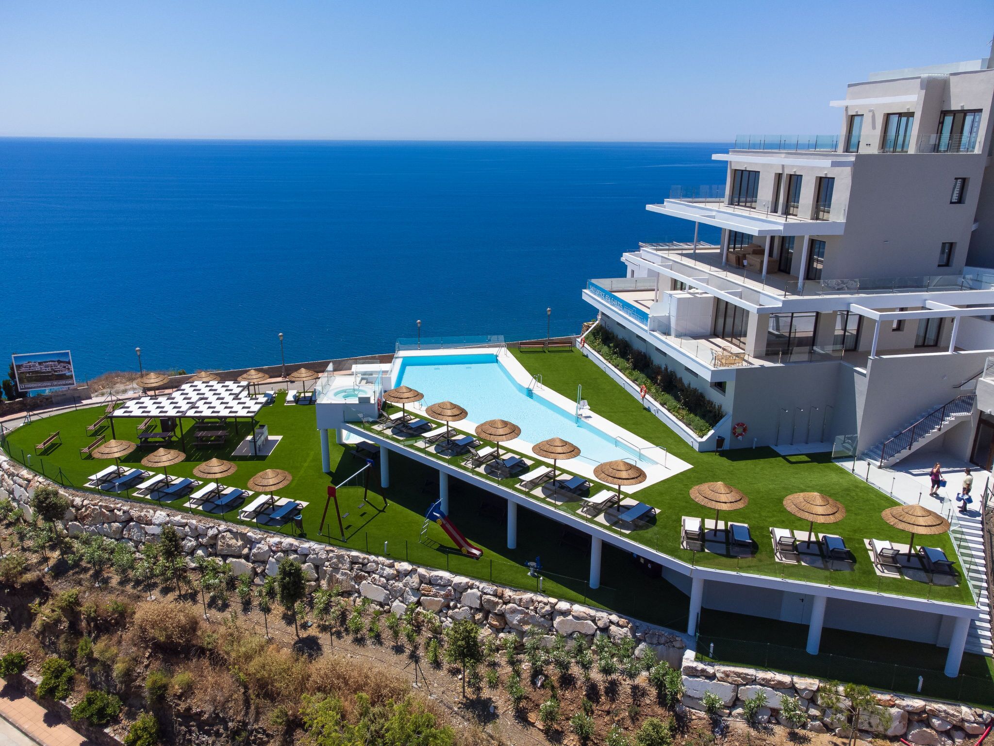 A modern hotel with a pool, sun loungers, and a view of the sea.