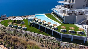A modern hotel with a pool, sun loungers, and a view of the sea.