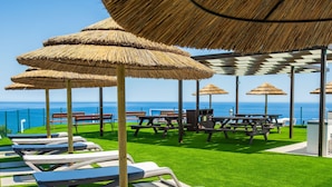A beachside patio with thatched umbrellas, lounge chairs, and picnic tables.