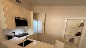 A modern kitchen with a built-in microwave, a coffee maker, and a sink. There is a window above the sink and a shelf with candles and books.
