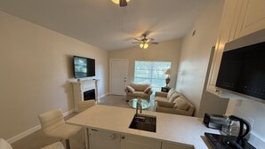 A modern kitchen with a central island, a dining area with a glass table, and a living room with a fireplace.
