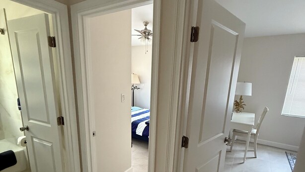 A room with a bed, a desk, and a chair. There is a door leading to another room.