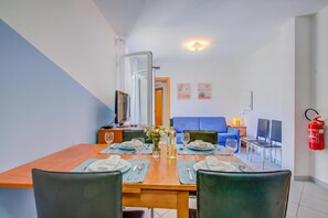 A dining area with a wooden table set for four, a blue sofa in the background, and a fire extinguisher mounted on the wall.