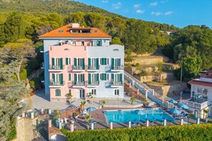 A multi-story hotel with a swimming pool, balconies, and a mountainous backdrop.