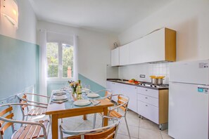 A compact kitchen with a dining area, white cabinets, a stove, and a window with a view of greenery.