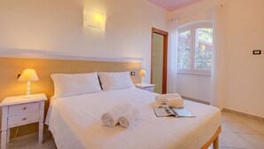 A hotel room with a bed, two bedside lamps, a window with curtains, a wooden headboard, and a magazine on the bed. - Seaview Pool Retreat - B6, Andora, Italy (Andora)
