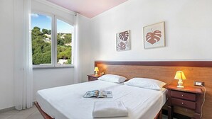 Une chambre d’hôtel comprenant un lit, deux tables de chevet, une fenêtre avec des rideaux et deux œuvres d’art murales.