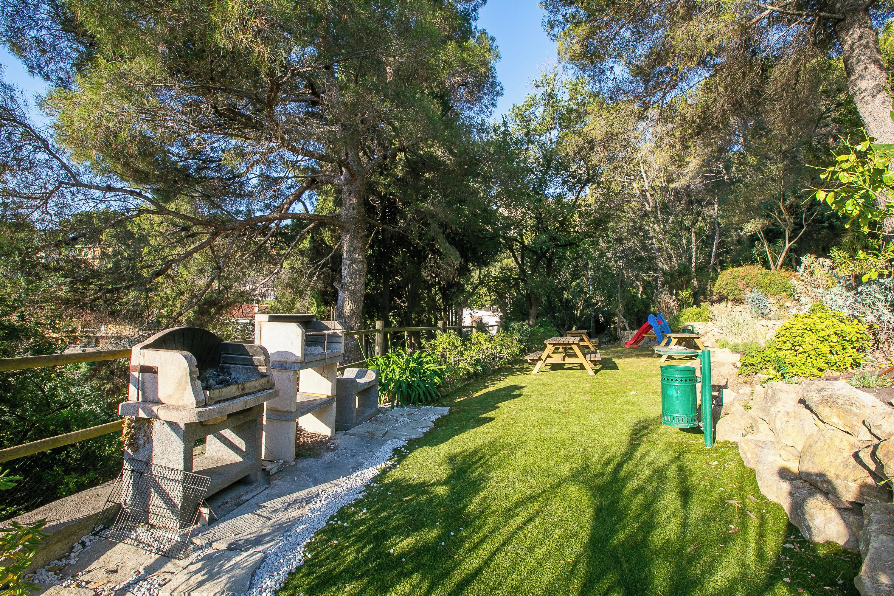 Un jardín bien cuidado con zona de barbacoa, un parque infantil y una mesa de picnic.