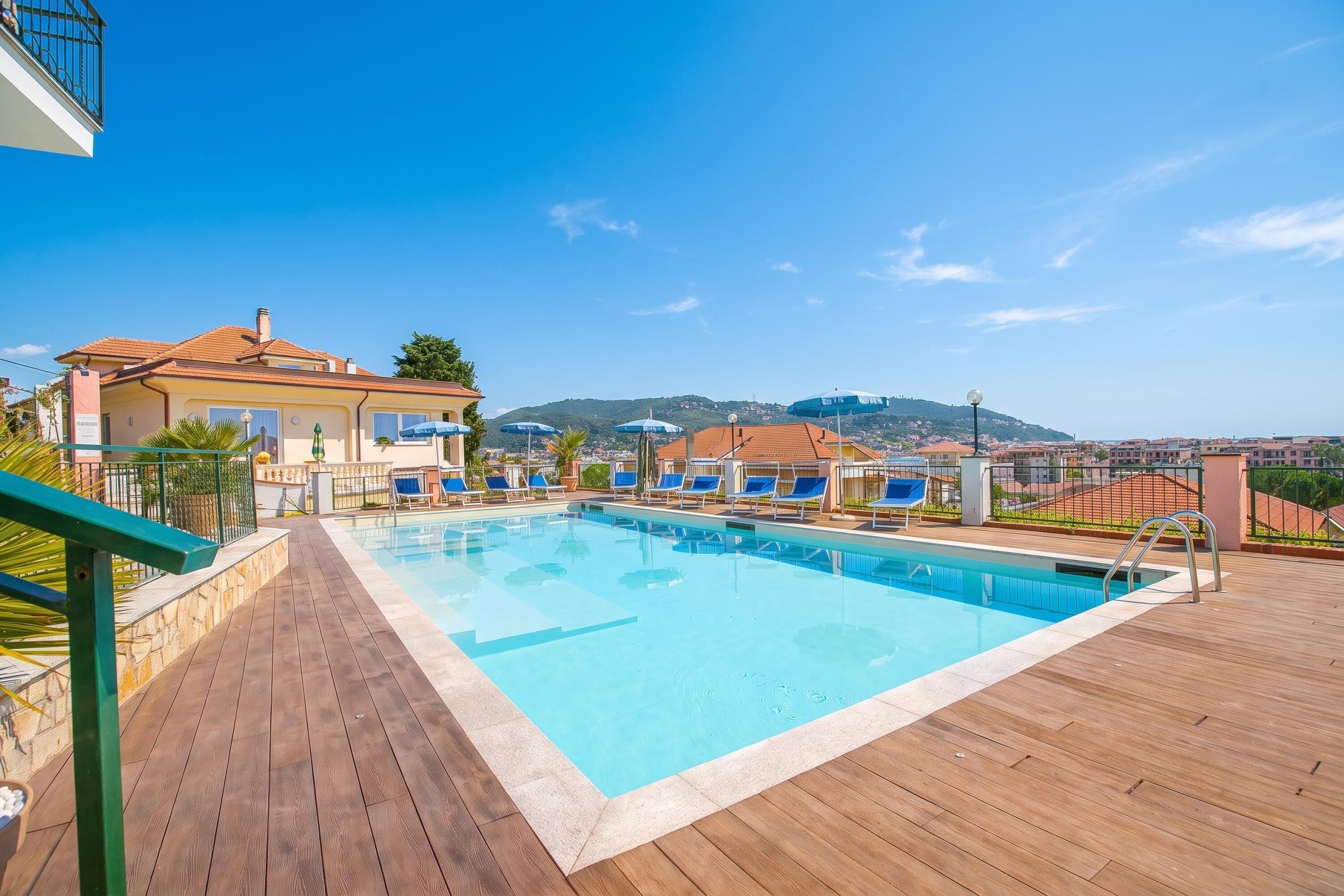 Ein Schwimmbecken mit Liegestühlen, einer Holzterrasse und Blick auf Hügel im Hintergrund.