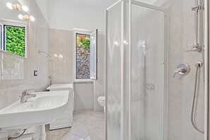 Ein modernes Badezimmer mit zwei Waschbecken, einer Dusche und einem Fenster mit Blick auf Grünflächen.