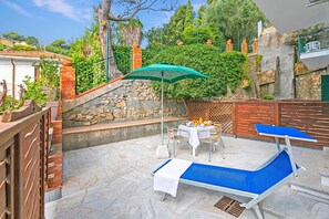 Eine Terrasse mit Tisch, Stühlen, einem blauen Liegestuhl und einem grünen Sonnenschirm.