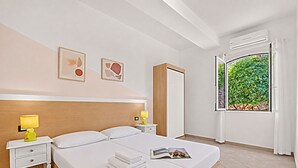 Une chambre d’hôtel comprenant un lit, deux tables de chevet avec lampes, une armoire et une fenêtre donnant sur un paysage verdoyant.