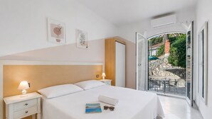 A bedroom with a bed, nightstands, a lamp, a book, and a view of an outdoor patio. - Seaview Pool Retreat - B1, Andora, Italy (Andora)