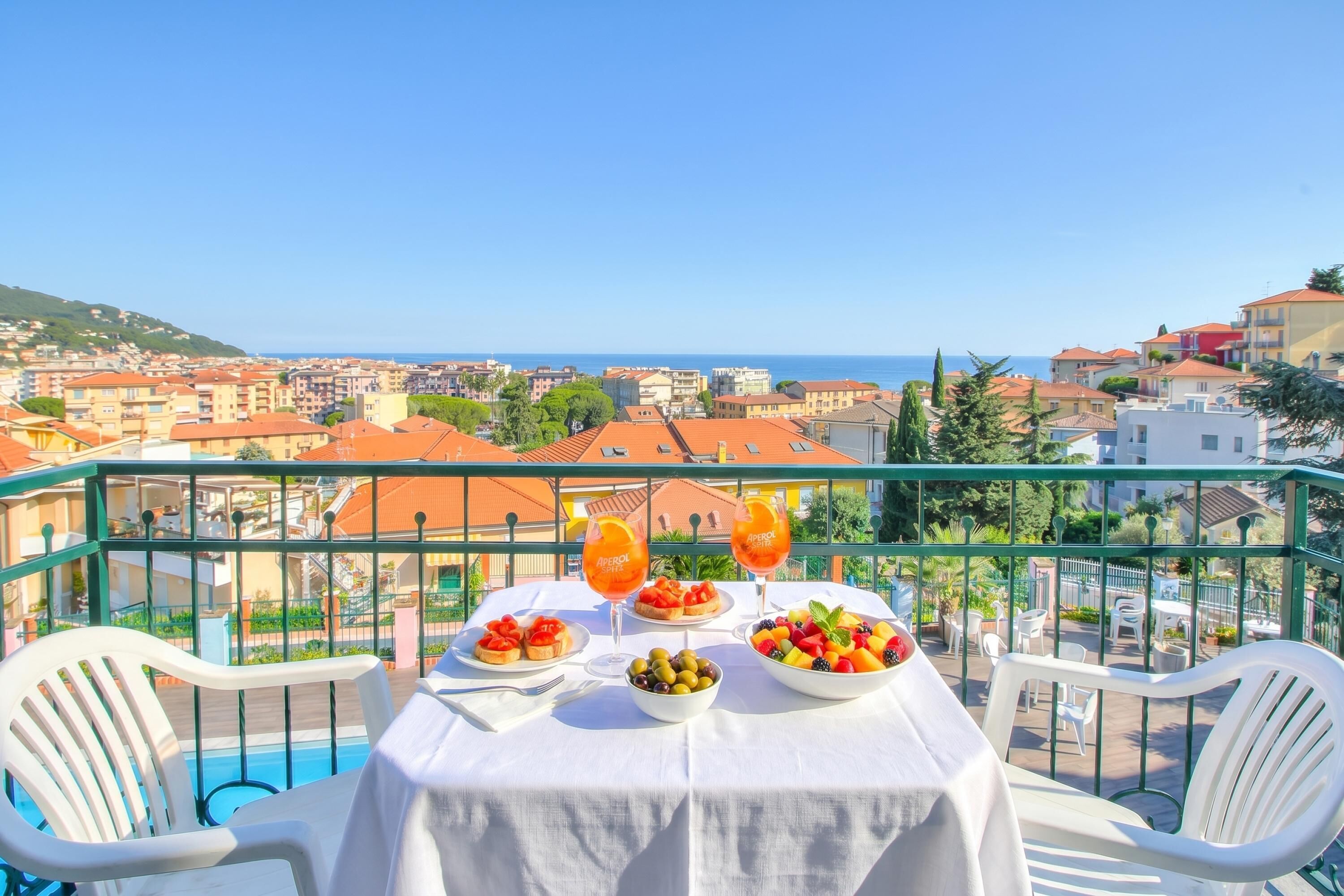 Una mesa con comida y bebidas en un balcón con vistas a un pueblo costero.