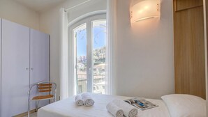 Ein Schlafzimmer mit Bett, Stuhl, Kleiderschrank und Fenster mit Blick auf Gebäude.