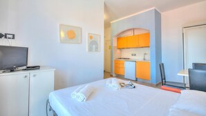 Ein Hotelzimmer mit einem Bett, einem Schreibtisch, einem Fernseher und einer Küchenzeile im Hintergrund.