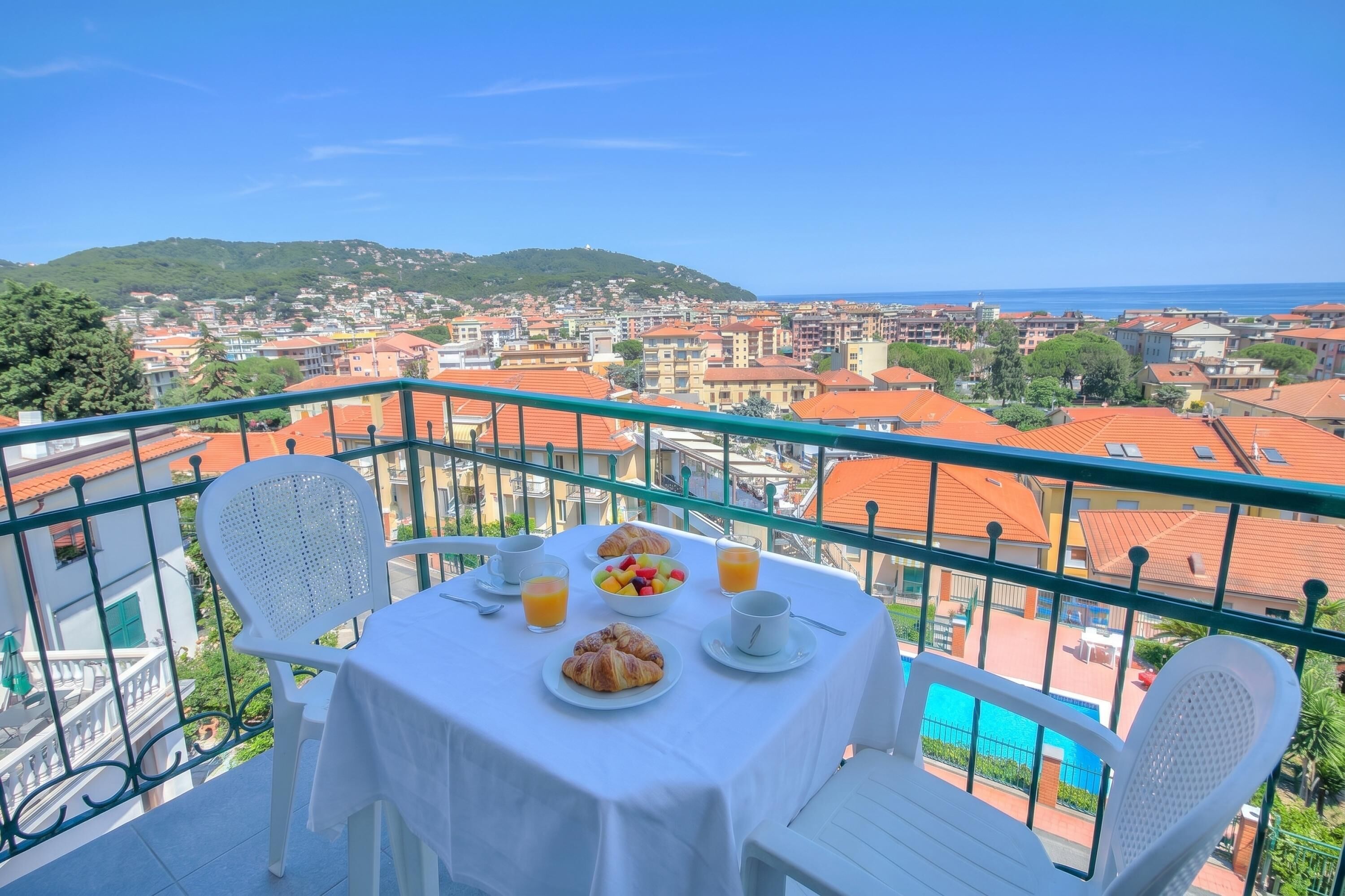 A balcony with a table set for breakfast, overlooking a cityscape and a body of water.