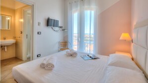 Une chambre d’hôtel comprenant un lit, une télévision, une fenêtre avec des rideaux, une lampe de chevet et une salle de bain avec un lavabo et un miroir.