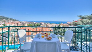 Un balcon avec une table préparée pour le petit-déjeuner, offrant une vue sur une ville côtière et la mer.
