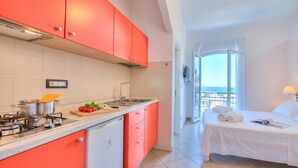 Une cuisine moderne avec des meubles rouges, une cuisinière et un évier. Il y a un balcon avec un lit et une vue.