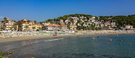 A coastal town with a beach, clear waters, and buildings with balconies.