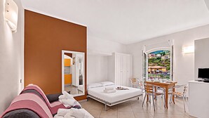 Une chambre d’hôtel comprenant un lit, un canapé, une table à manger avec des chaises, une télévision et une vue sur un village par la fenêtre.