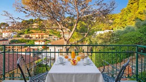 Une table de balcon dressée pour le petit-déjeuner, avec vue sur un quartier résidentiel bordé d’arbres et de maisons.