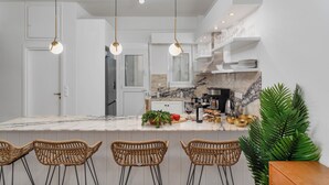 A modern kitchen with a marble countertop, hanging pendant lights, wicker bar stools, and a potted plant. - Athens City Views - 4BR Luxury w/ Chef's Kitchen & Balconies (Athina)