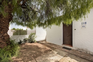 A white building with a brown door, a number '51B' and 'AL' sign, and a tree in front.
