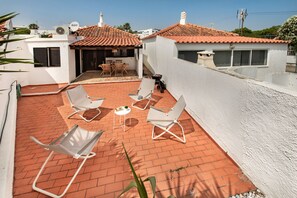 A rooftop patio with white walls, red-tiled roof, and several white lounge chairs.